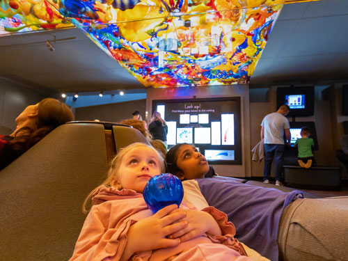 Children looking up  at the colorful ceiling created by Fireworks of Glass sculpture.